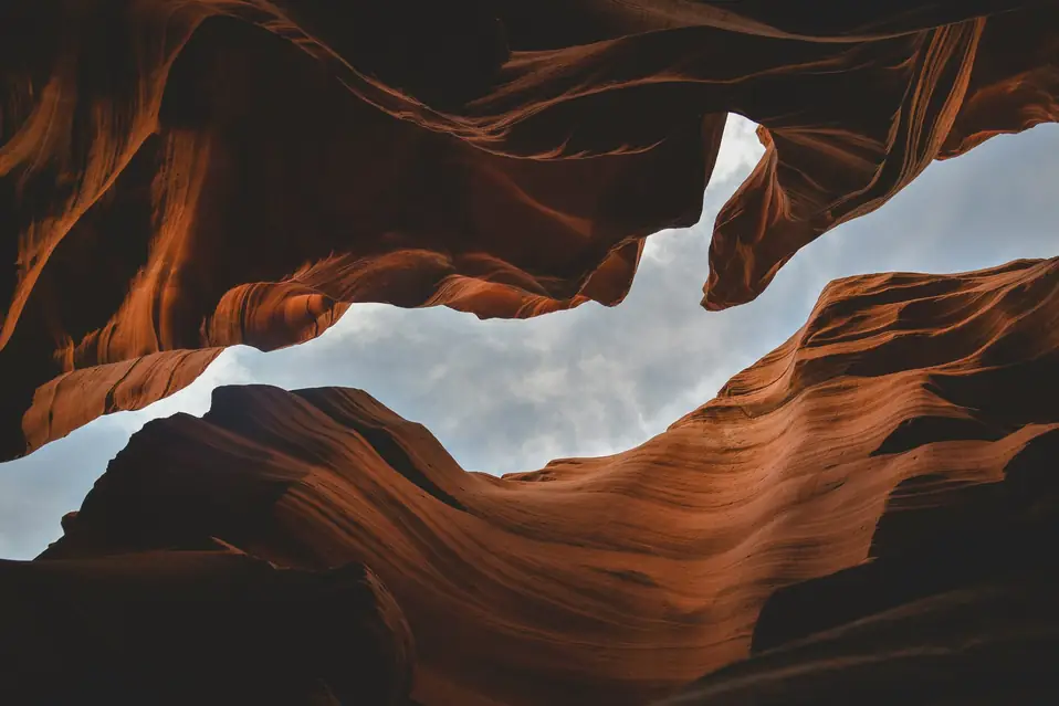 Looking up through curved sandstone canyon walls toward a narrow strip of cloudy sky
