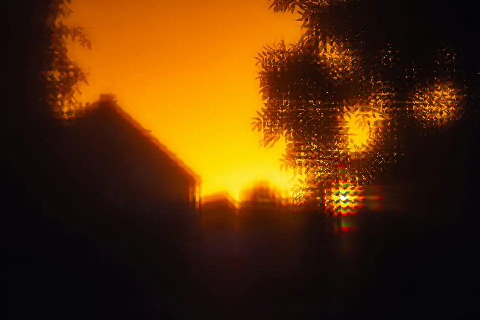 Soft-focus sunset behind a house roof and tree silhouette, standing in for Shopify prices and fees that change once a buyer’s destination comes into view