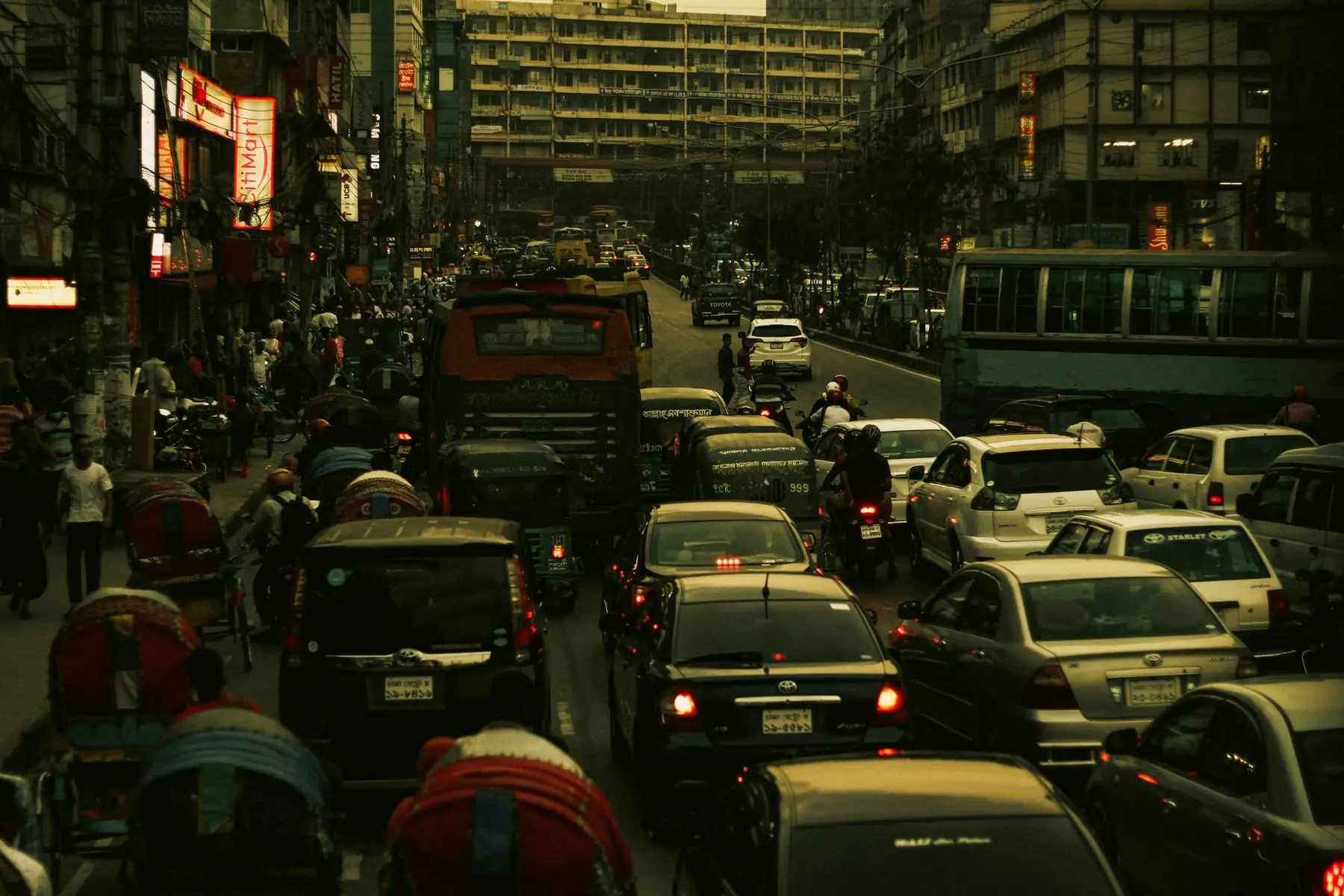 Evening traffic jam packed with rickshaws, cars, buses, and red brake lights on a dense urban street